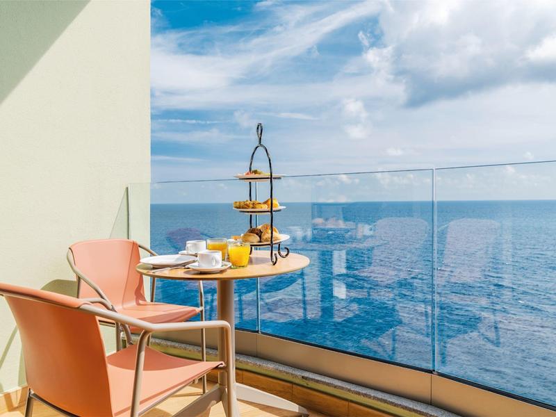 Balkon mit Tisch, Stühlen und Blick auf das Meer unter blauem Himmel.