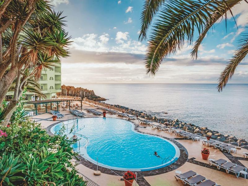 Poolbereich mit Palmen und Blick auf das Meer bei klarem Himmel.