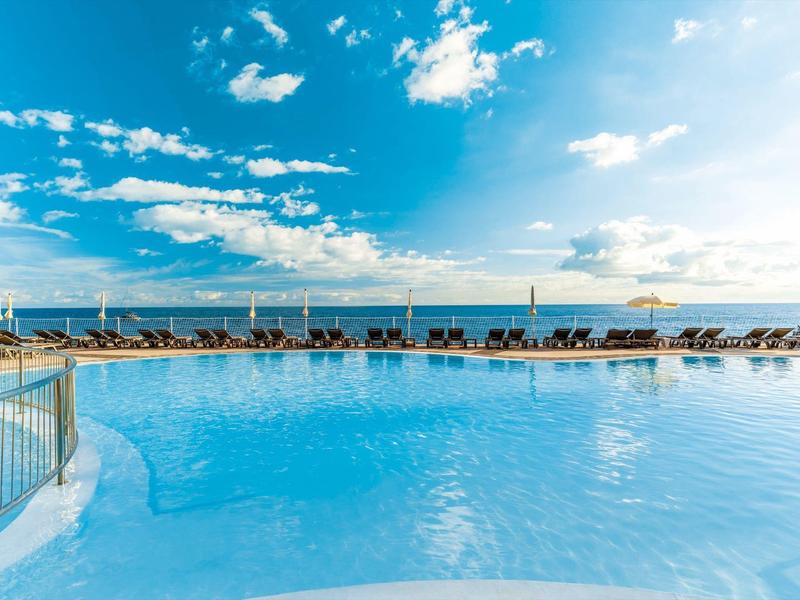 Großer Pool mit Liegestühlen und klarem Himmel am Meeresufer.