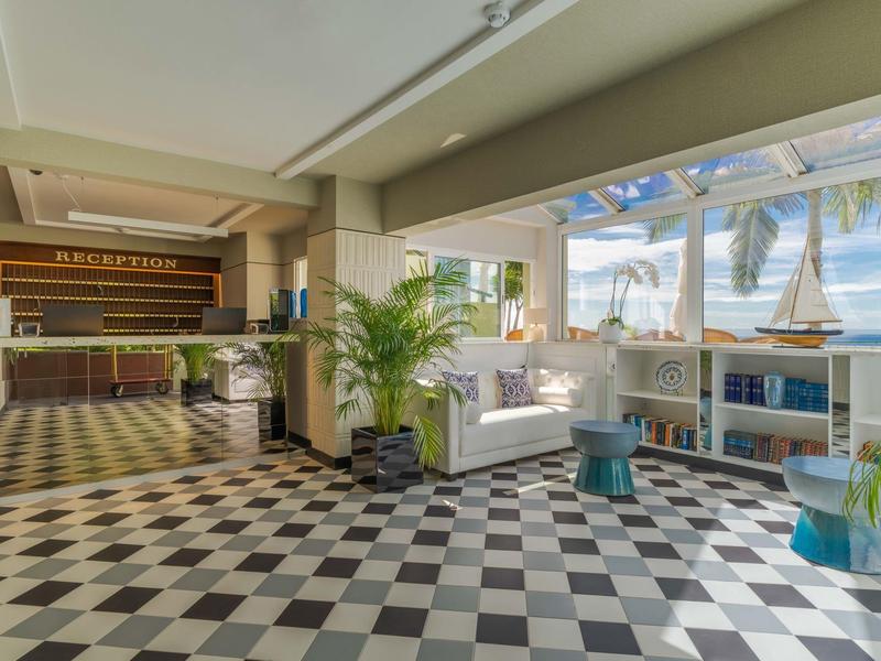 Helle Hotellobby mit Schachbrettboden, Empfangstresen und maritimen Dekorationen am Fenster.