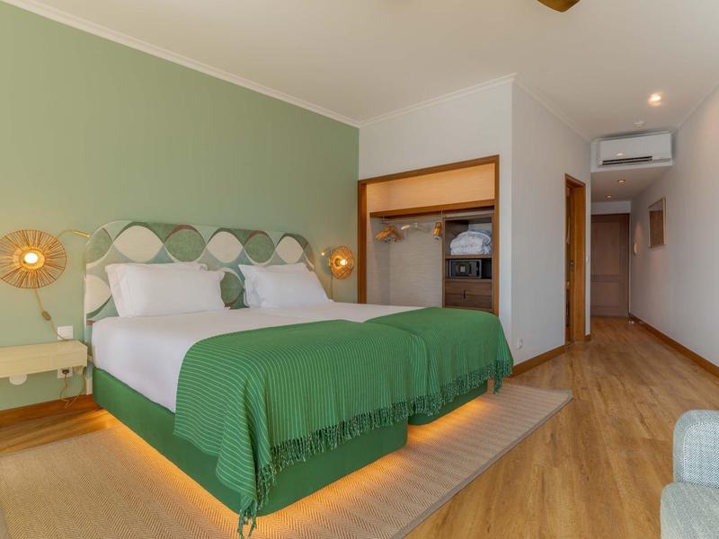 Modern eingerichtetes Hotelzimmer mit großem Doppelbett und grünem Bettüberwurf.