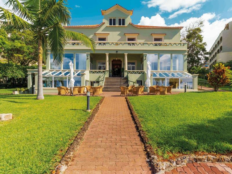 Großes Ferienhaus mit Terrasse und Garten unter blauem Himmel.