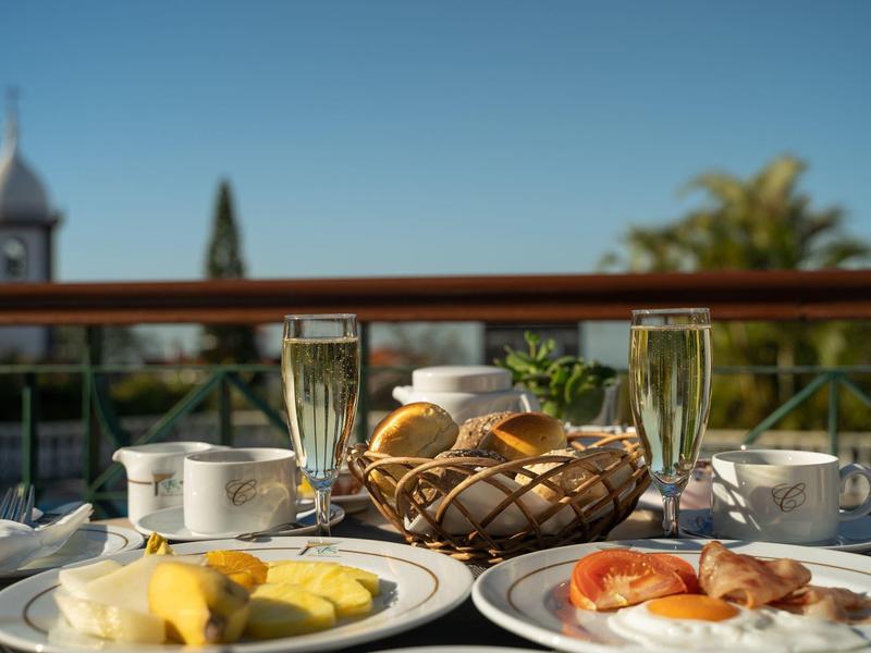 Ein gedeckter Frühstückstisch mit Brötchenkorb, Kaffee, Orangensaft und Tellern mit Speck, Ei und Ananas.