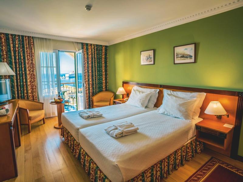 Gemütliches Hotelzimmer mit zwei Betten, grüner Wand und Balkon mit Ausblick.