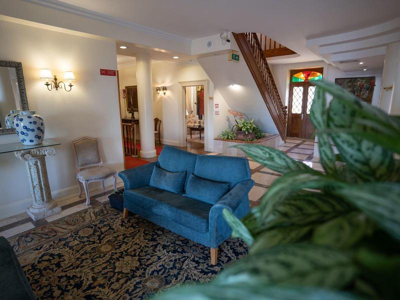 Wohnzimmer mit blauem Sofa, Teppich, Pflanzen, Treppe und weißen Wänden im klassischen Stil.