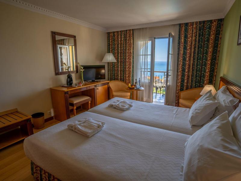 Gemütliches Hotelzimmer mit zwei Einzelbetten, Schreibtisch, Fernseher und Balkon mit Meerblick.
