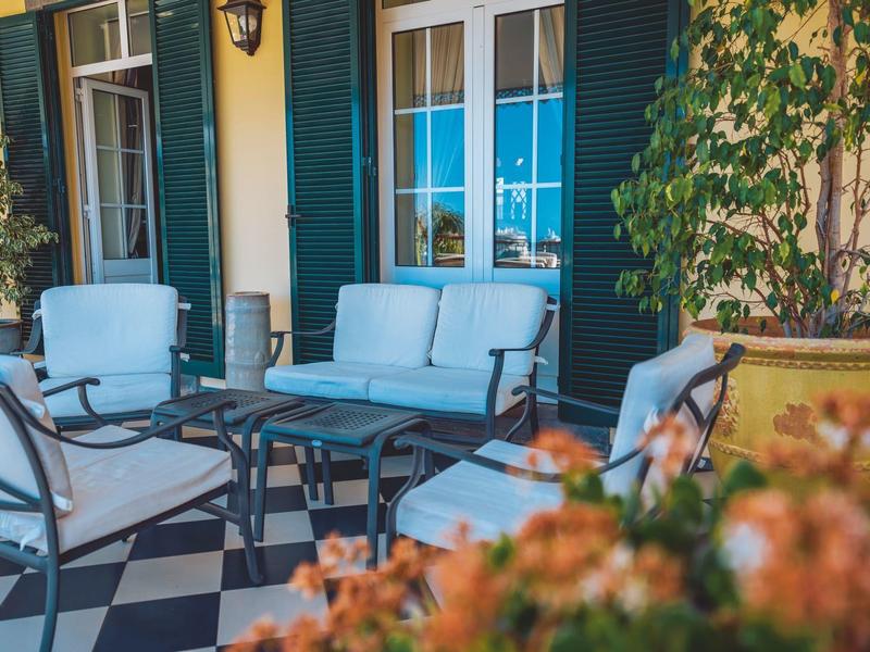 Gemütliche Terrasse mit blau gepolsterten Sesseln, Glashaustisch und grünem Pflanzenbewuchs.