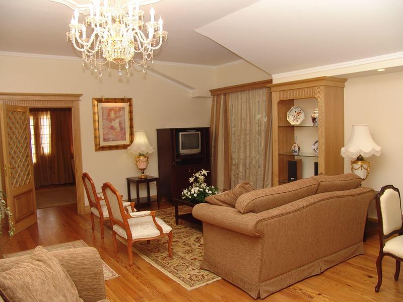 Gemütliches Wohnzimmer mit braunen Sofas, Holzstühlen, Teppich und Kronleuchter an der Decke.