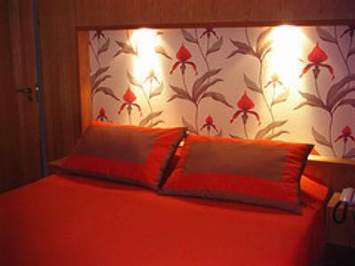 Tweepersoonsbed met rode kussens en beddegoed voor bloemmotiefbehang en wandverlichting.