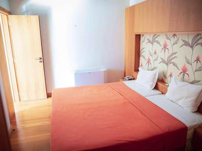 Licht ingericht hotelkamer met tweepersoonsbed en bloemenpatroon op het hoofdeinde.