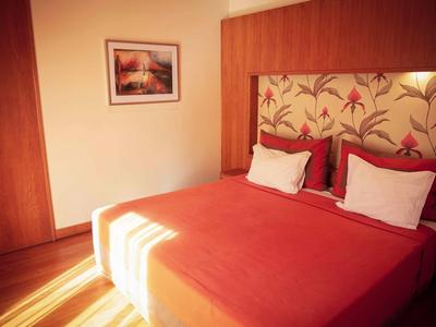 Habitación de hotel acogedora con cama doble, colcha roja y cabecera floral.