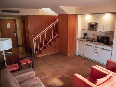 Gezellige woonkamer met keukenhoek, trap en zitgelegenheid in warme kleuren.