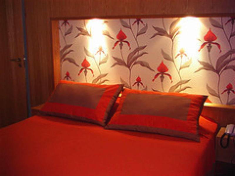 Tweepersoonsbed met rode kussens en beddegoed voor bloemmotiefbehang en wandverlichting.