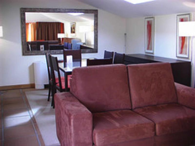 Gezellige woonkamer met bordeauxrode bank, zwarte eethoek en grote wandspiegel.