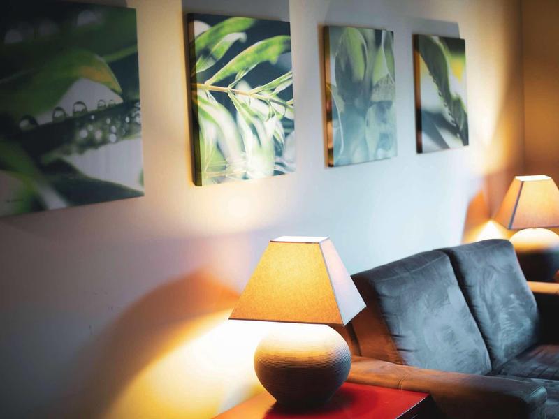 Gezellige woonkamer met lampen, bank en plantenfoto's aan de muur.