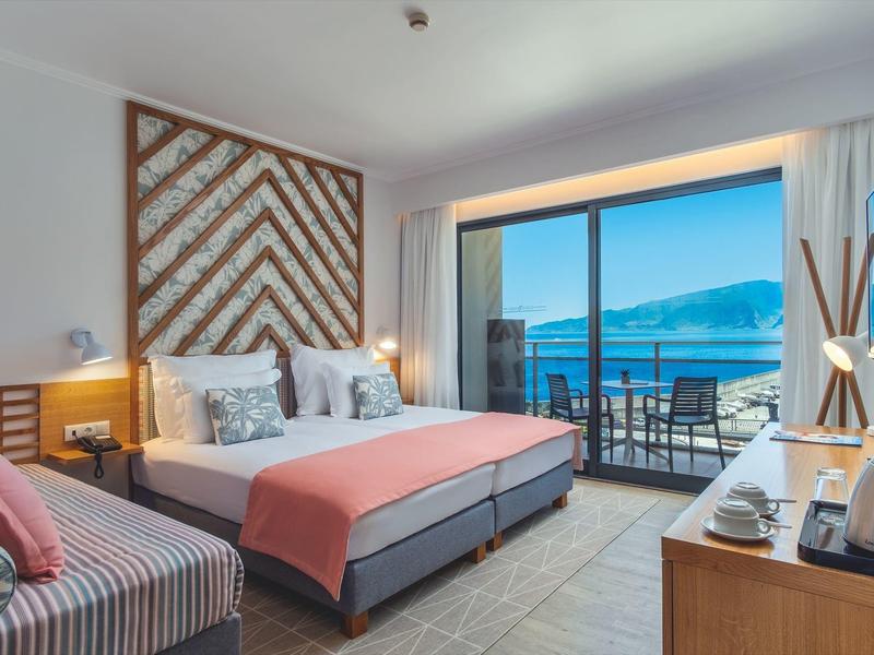 Helles Zimmer mit Doppelbett, Balkon, Blick aufs Meer und gemütlicher Einrichtung in warmen Farben.
