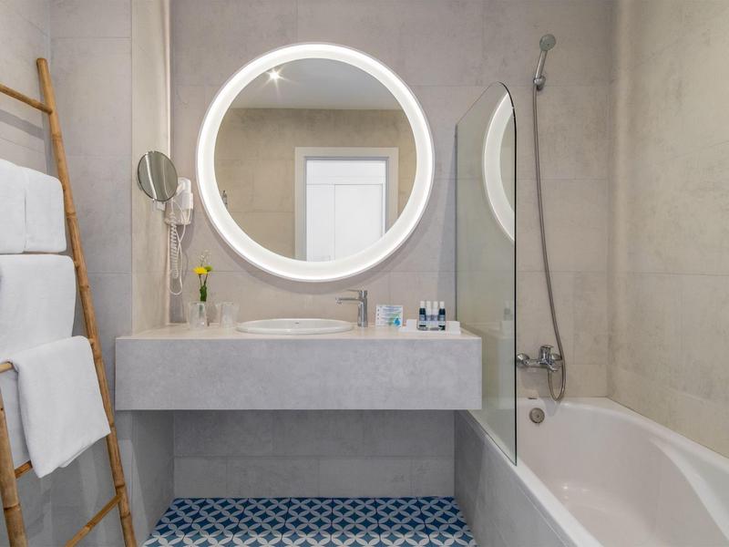 Modernes Badezimmer mit runder beleuchteter Spiegel, grauem Waschbecken und Badewanne.