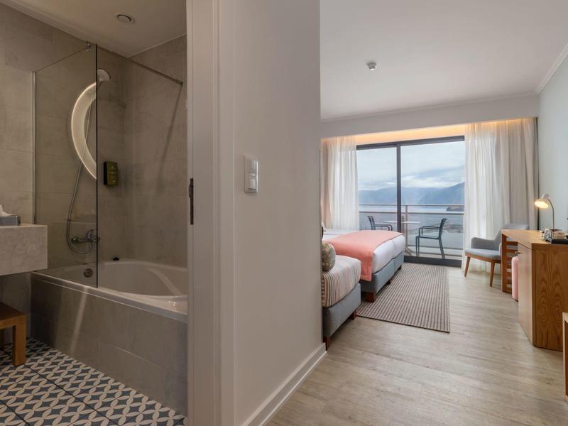 Modernes Hotelzimmer mit Doppelbett, Balkon mit Meerblick und angrenzendem Badezimmer mit Badewanne.