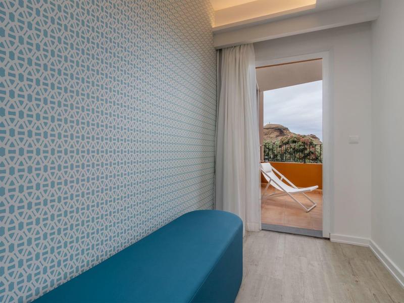 Schmaler Raum mit blauem Sitz und gemusterter Wand, offener Tür zum Balkon mit Landschaft.