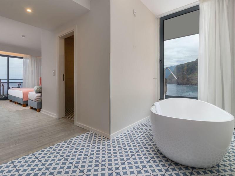 Modernes Badezimmer mit freistehender Badewanne auf gemusterten Bodenfliesen und angrenzendem Schlafzimmer.