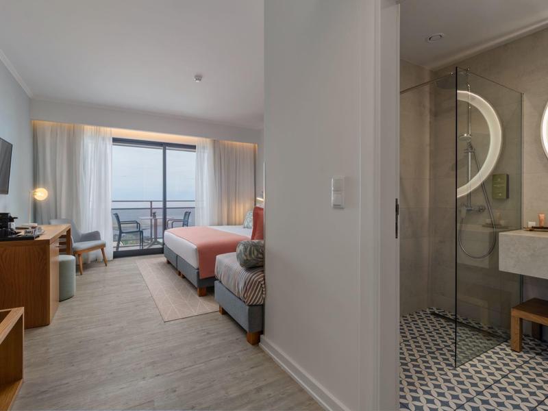 Modernes Hotelzimmer mit bequemen Betten, Balkon, TV und einem hellen Badezimmer mit Glasdusche.