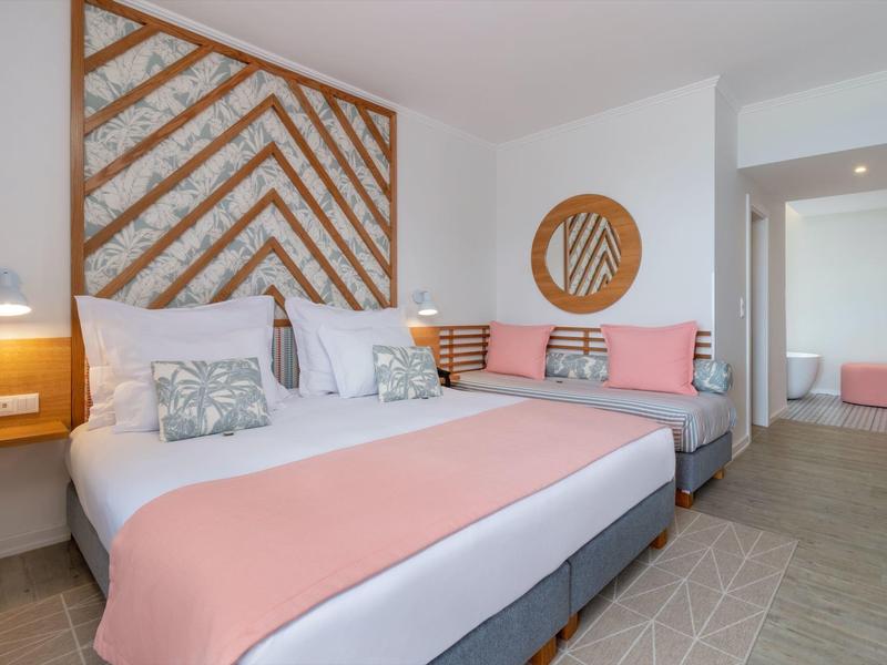 Modernes Hotelzimmer mit großem Bett, rosafarbenen Akzenten und Holzdekor an der Wand.