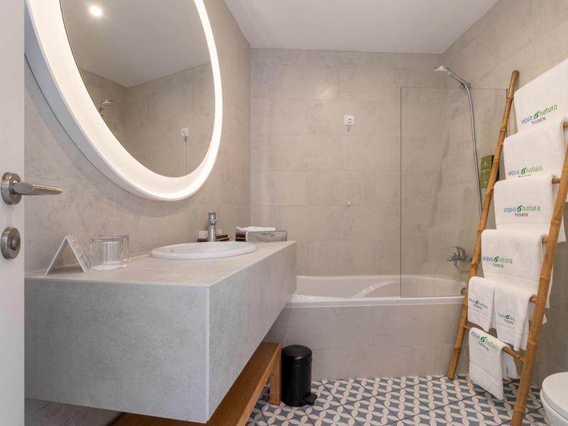 Modernes Badezimmer mit grauen Wänden, beleuchtetem runden Spiegel und Badewanne mit Duschvorhang.