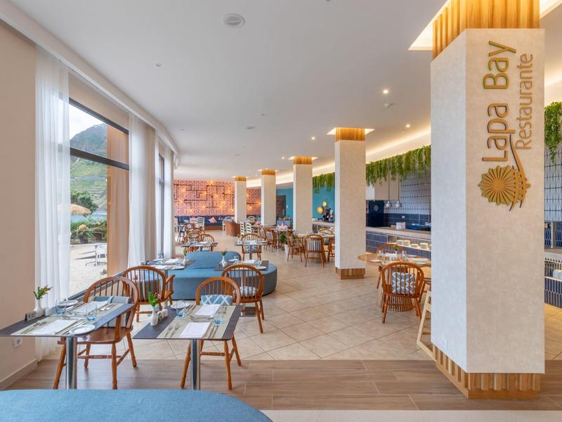 Moderner Essbereich mit Windschutz, Holzmöbeln, blauen Kissen und grünen Pflanzen an der Decke.