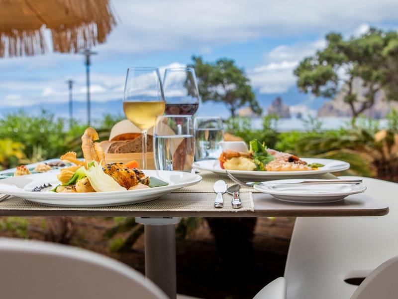 Outdoor-Tisch mit gedeckten Tellern, Gläsern, Besteck und Sommeressen bei sonnigem Wetter.