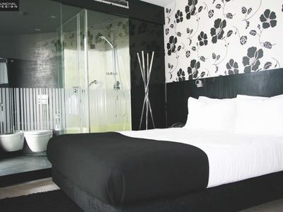 Camera d'hotel moderna con letto matrimoniale, arredamento in bianco e nero e doccia in vetro.