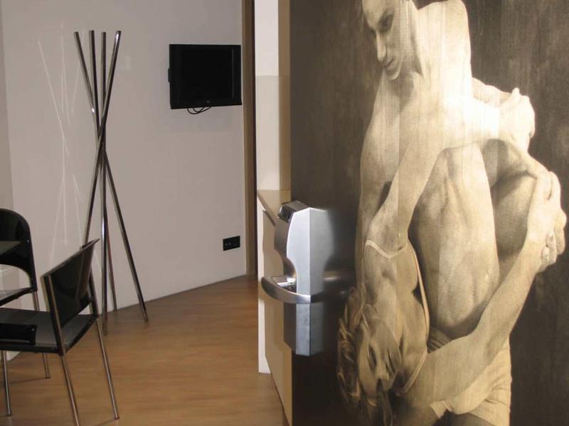 Hall d'hotel moderno con pavimento in legno, sedie nere e grande murale a tema danza.
