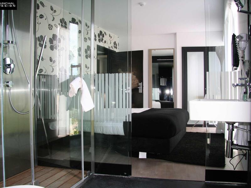 Camera d'hotel moderna con doccia in vetro, letto nero e pareti bianche.