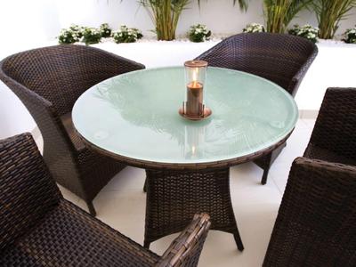 Tavolo in vetro moderno con candela circondato da quattro sedie intrecciate sul balcone.