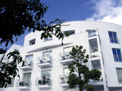 Edificio di hotel bianco moderno con balconi e alberi davanti sotto un cielo blu.