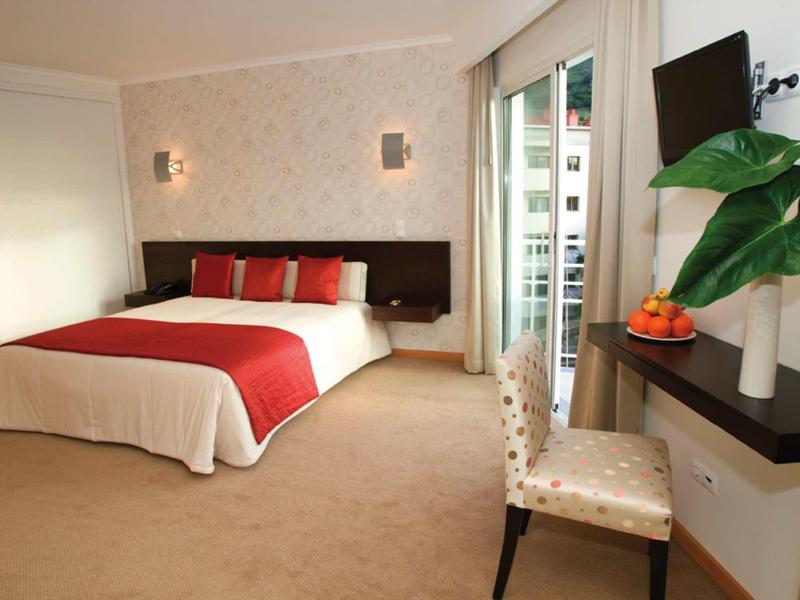 Camera d'hotel moderna con letto matrimoniale, TV e scrivania accanto a una grande finestra.