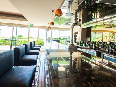 Moderner Barbereich mit glänzendem Holztheken, blauen Sitzbänken und großen Fenstern.