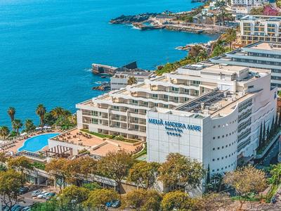 Großes Hotel an Küste mit blauem Meer, Pool, Palmen und umliegenden Gebäuden bei klarem Himmel.