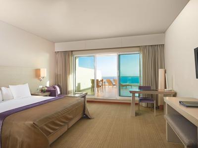 Helles Hotelzimmer mit großem Bett, Schreibtisch, Balkon und Blick auf das Meer.