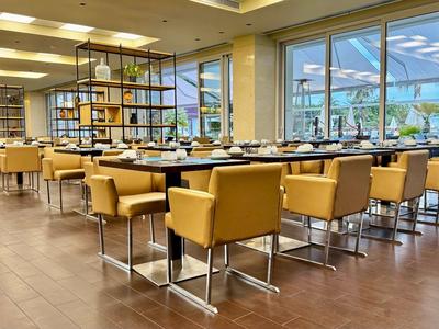 Modern hotel restaurant with yellow chairs and large windows overlooking the terrace.