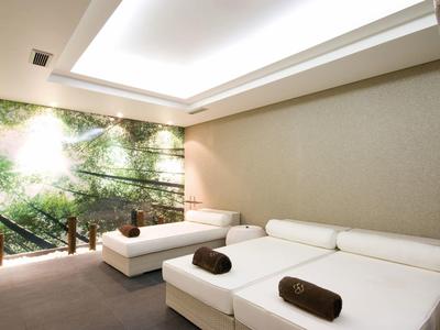 Ruheraum mit zwei weißen Liegen, grüner Wandgestaltung und sanftem Deckenlicht.