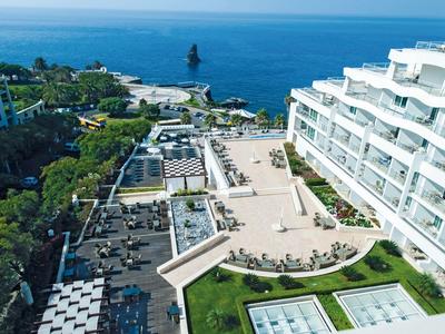 Moderner Hotelkomplex mit weißem Gebäude, Terrasse, Pool und Blick auf das blaue Meer.