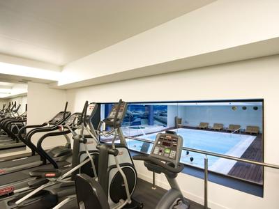 Vue d'une salle de sport avec des tapis roulants et une piscine visible à travers une fenêtre