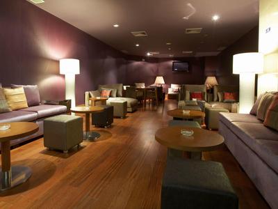 Langer, gemütlicher Raum mit Holzboden, Sofas, Tischen, Hockern und warmen Lampen an der Wand.