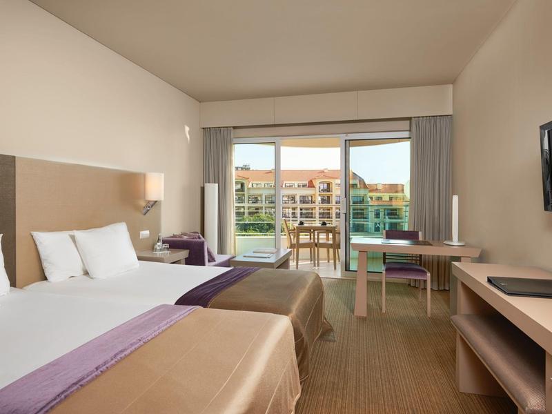 Hell eingerichtetes Hotelzimmer mit zwei Betten, Balkon und modernem TV an der Wand.