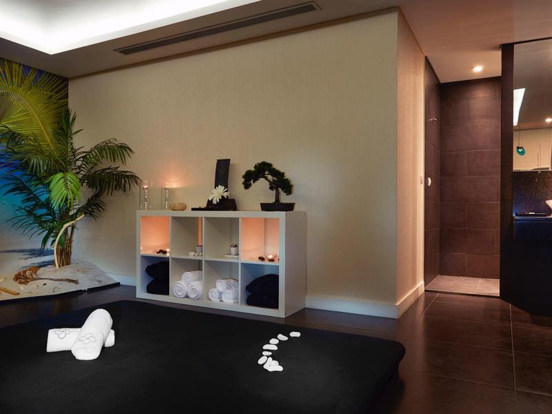 Moderner Wellnessraum mit schwarzer Liege, weißem Regal, Pflanzen und stimmungsvoller Beleuchtung.