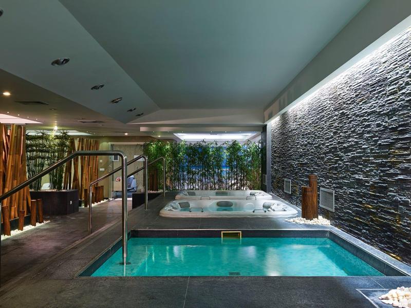 Moderner Wellnessbereich mit Pool, Whirlpool, Natursteinwand und indirekter Beleuchtung.