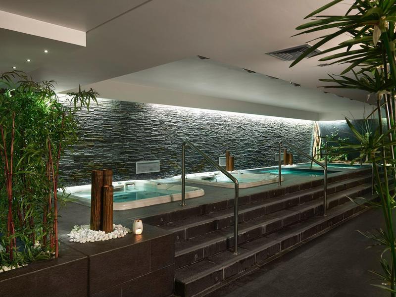 Moderner Spa-Bereich mit beleuchtetem Pool, Steinwand und grünen Pflanzen in ruhiger Atmosphäre.