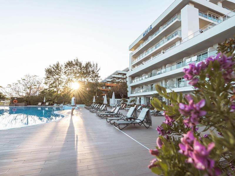 Sonnenuntergang am Pool mit blühenden Blumen und Liegestühlen neben einem Hotelgebäude.