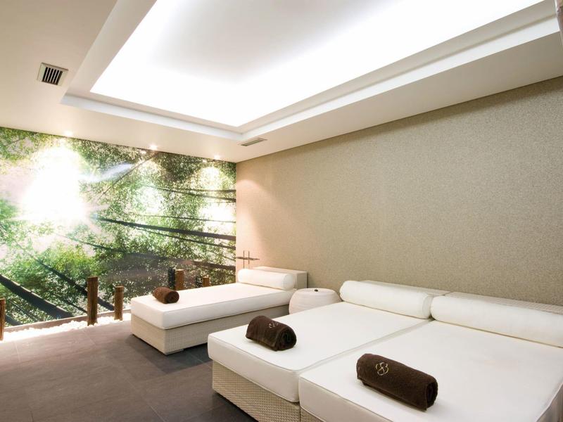 Ruheraum mit zwei weißen Liegen, grüner Wandgestaltung und sanftem Deckenlicht.