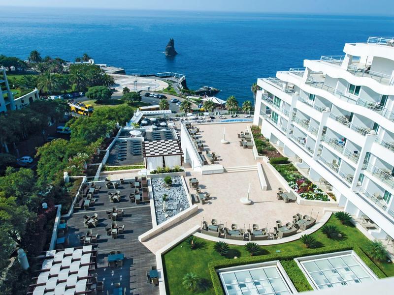 Moderner Hotelkomplex mit weißem Gebäude, Terrasse, Pool und Blick auf das blaue Meer.